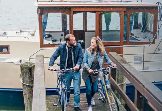 ein Paar verlässt das Hausboot über einen Steg mit je einem Fahrrad