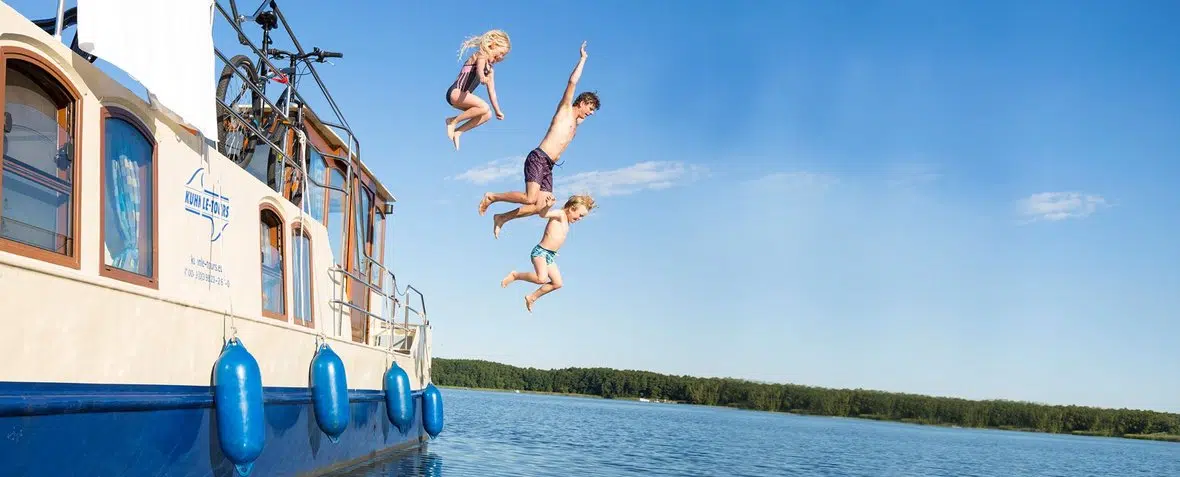 3 Kinder hopsen von einem Hausboot ins Wasser