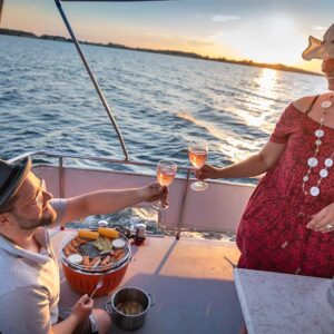 Ein Paar bim grillen auf der Babro Beluga. Beide halten ein Glas Champagner in der Hand und stoßen an.