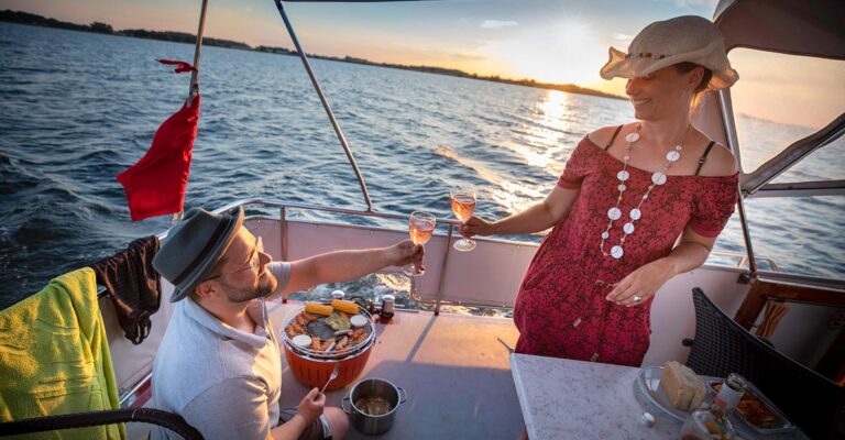 Ein Paar bim grillen auf der Babro Beluga. Beide halten ein Glas Champagner in der Hand und stoßen an.