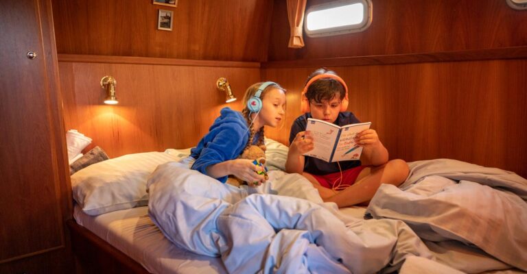 Zwei Kinder teilen sich ein Doppelbett in der Babro Beluga. Sie sitzen auf dem Bett mit Kopfhörern und lesen gemeinsam ein Buch.