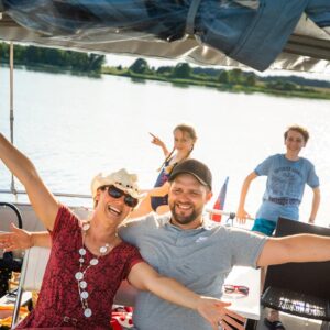 Eine Familie auf dem Sonnendach einer Babro Beluga. Die Eltern sind im Vordergrund am Steuer, die Kinder sind im Hintergrund und genießen das Sommerwetter.