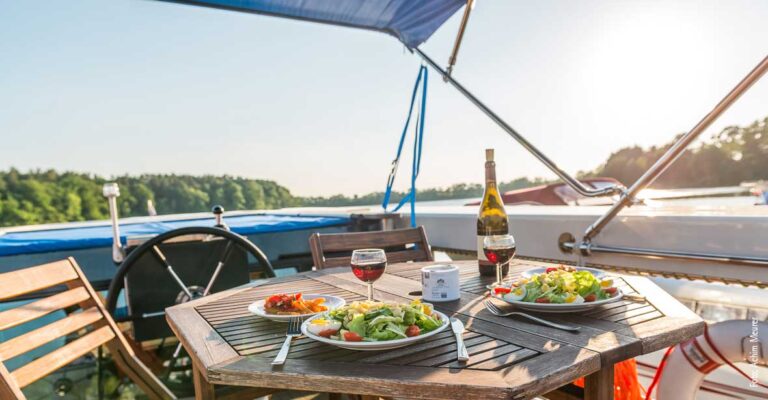 an Deck der Aquino steht ein hübscher Holztisch, gedeckt mit Salat und Wein, darüber ist das Bimini gespannt gegen die Sonne