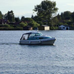 die Bellus fährt über einen See, im Hintergrund sind Bootshäuser