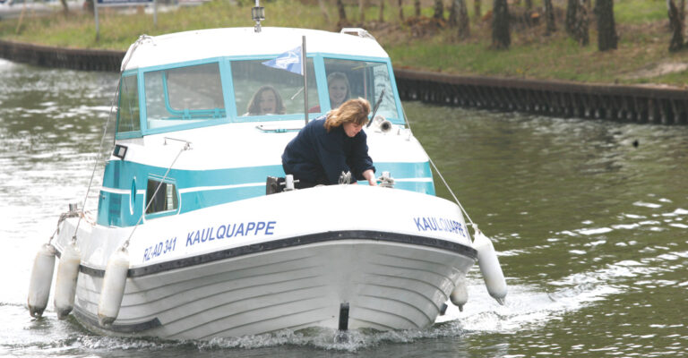 ein Boot fährt durch einen Kanal, an Deck sind 3 Frauen