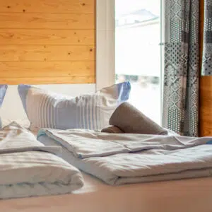Ein bereits bezogenes Doppelbett in einer Schlafkabine eines Pedro H2Home. Die Kissen und decken sind mit einem blau-weißen Bezug bezogen.