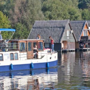 Eine Kormoran fährt an einer reihe Bootshäuser vorbei.