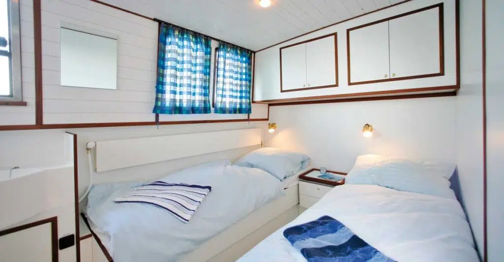 Eine Kabine in einer Kormoran mit zwei Betten. Die Betten sind mit weiß gestreiften Bezügen bezogen.