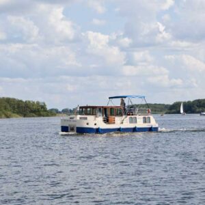 Seitenansicht einer Kormoran. Ein blau-beiges Boot in Fahrt auf der Müritz.