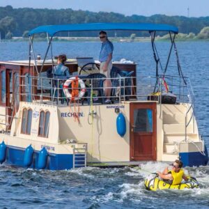 Ein Paar auf einer Kormoran 1150. Hinter der Kormoran hängt eine Person auf einer Tube, einem aufblasbaren Wasserschlitten.