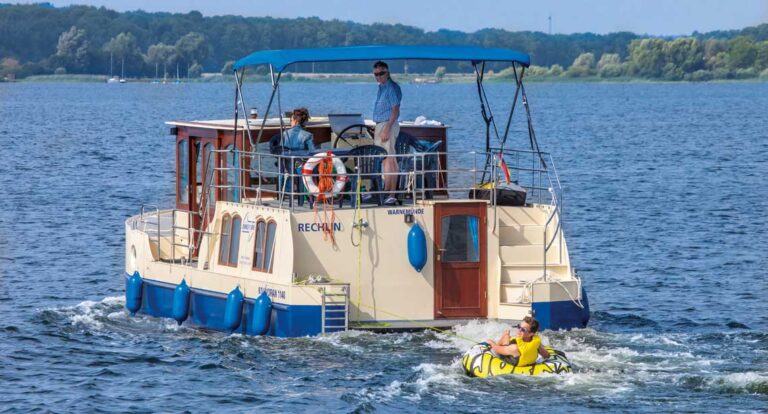 Ein Paar auf einer Kormoran 1150. Hinter der Kormoran hängt eine Person auf einer Tube, einem aufblasbaren Wasserschlitten.