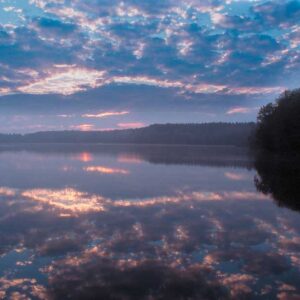 Ein leicht bewölkter Sonnenuntergang der sich im Wasser spiegelt.