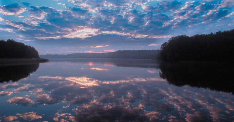 Ein leicht bewölkter Sonnenuntergang der sich im Wasser spiegelt.