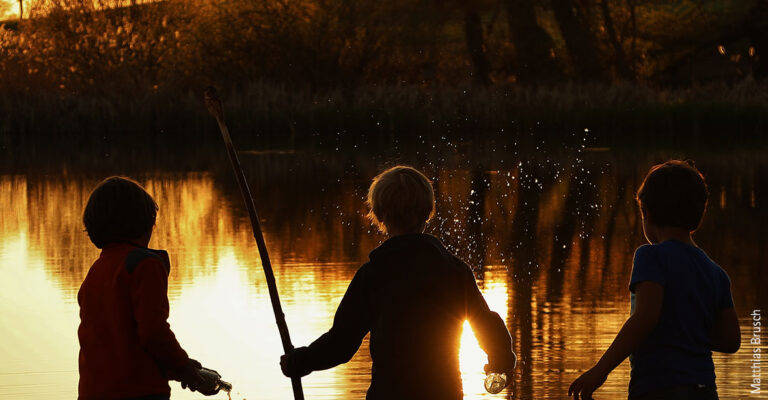 Drei Kinder spielen an einem Fluss bei Sonnenuntergang