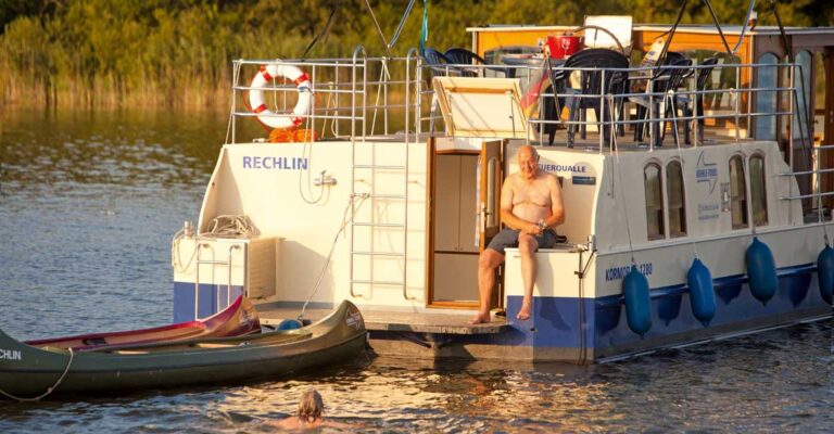 Ein Mann sitzt auf der Badeplattform einer Kormoran 1280. Neben der Kormoran sind zwei Kanus