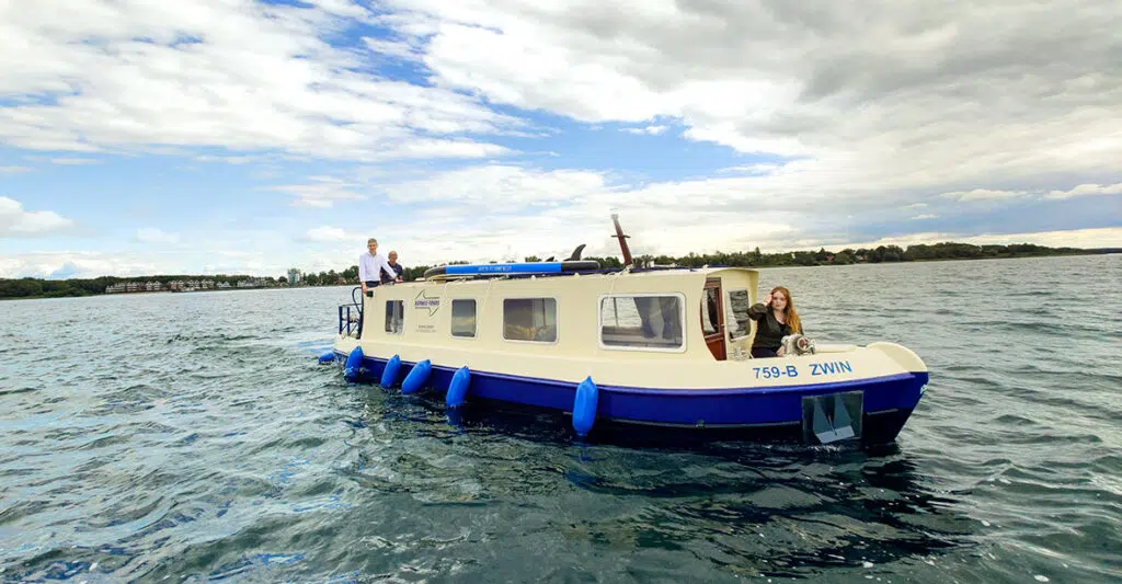 Kuinder auf der Müritz. Eine Person Sitzt auf dem Bug, zwei personen stehen hinten auf dem Heck.