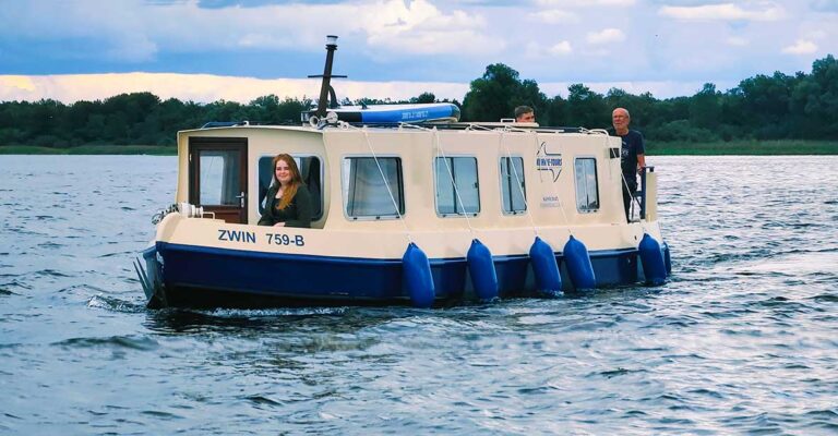 Kuinder auf der Müritz. Eine Person Sitzt auf dem Bug, zwei personen stehen hinten auf dem Heck.