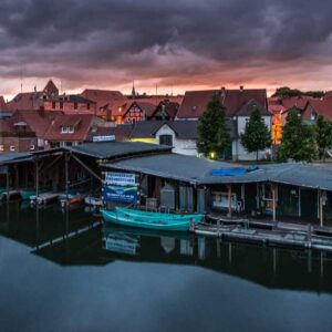 Luftaufnahme mit einer Reihe Bootshäuser, u.A das der Müritzfischer. im Hintergrund ist die Stadt Plau am See zu sehen.