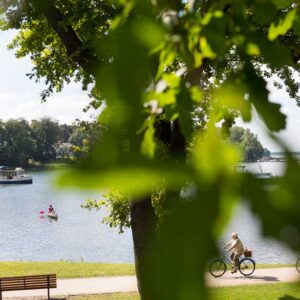 Ein Radweg der am Wasser entlang führt, zwei Radfahrer fahren gerade entlang.