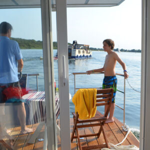 Vater und Sohn stehen auf der Veranda des Febo720 Cabin. Der Sohn lehnt sich an die Reling und der Vater steht am Steuer.