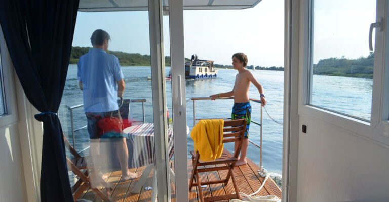 Vater und Sohn stehen auf der Veranda des Febo720 Cabin. Der Sohn lehnt sich an die Reling und der Vater steht am Steuer.