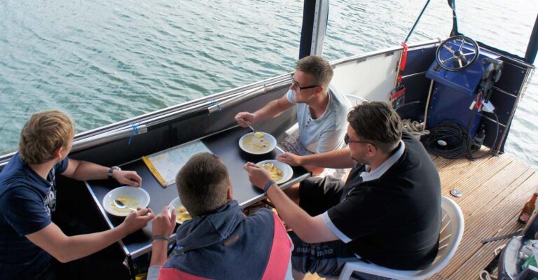 Eine Gruppe sitzt an einem Campingtisch auf dem Febo720 open und isst Suppe.