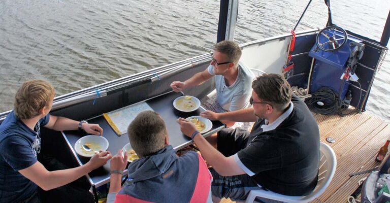 Eine Gruppe sitzt an einem Campingtisch auf dem Febo720 open und isst Suppe.