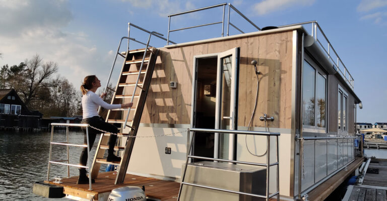 Heckansicht des Saunahausbootes. Eine Frau klettert die Treppe zur Dachterrasse hoch.