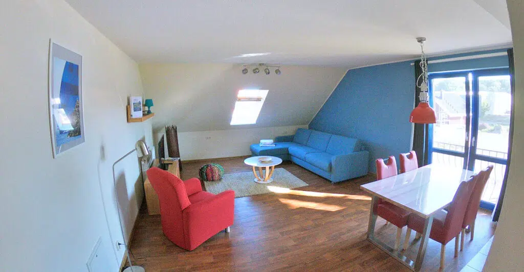 Geräumiges Wohnzimmer mit Couch, Sessel, Fernseher und Tür zum Balkon.