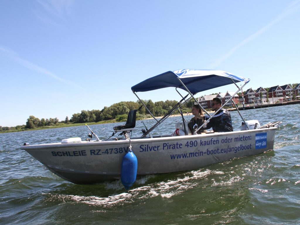 ein kleineres Motorboot fährt durch die Wellen der Müritz, im Hintergrund das Hafendorf