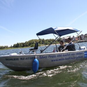 ein kleineres Motorboot fährt durch die Wellen der Müritz, im Hintergrund das Hafendorf